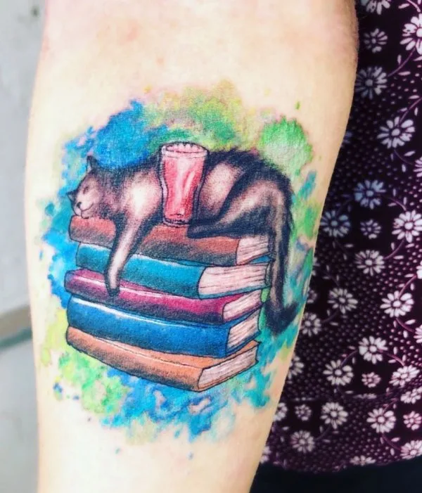 Cat sleeping on books inked on inner arm.