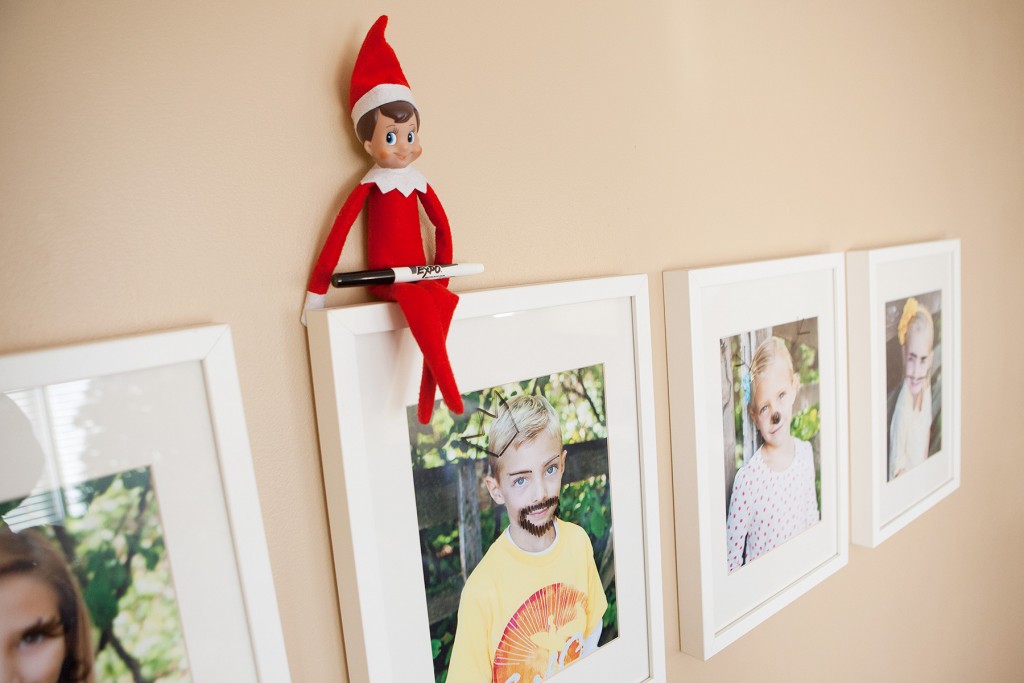 Elf draws silly faces on framed photos with dry erase marker.