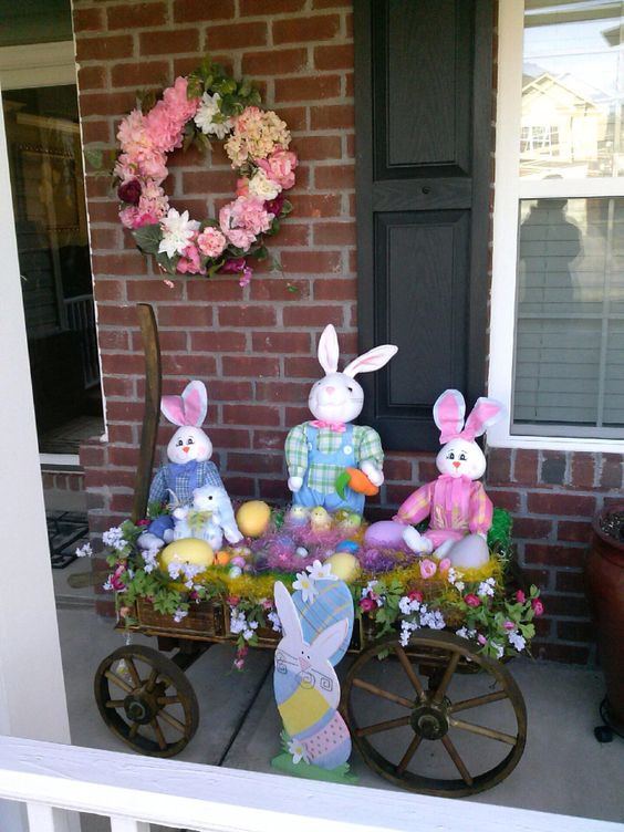 Bunnies are sitting in the cart with eggs and flowers.