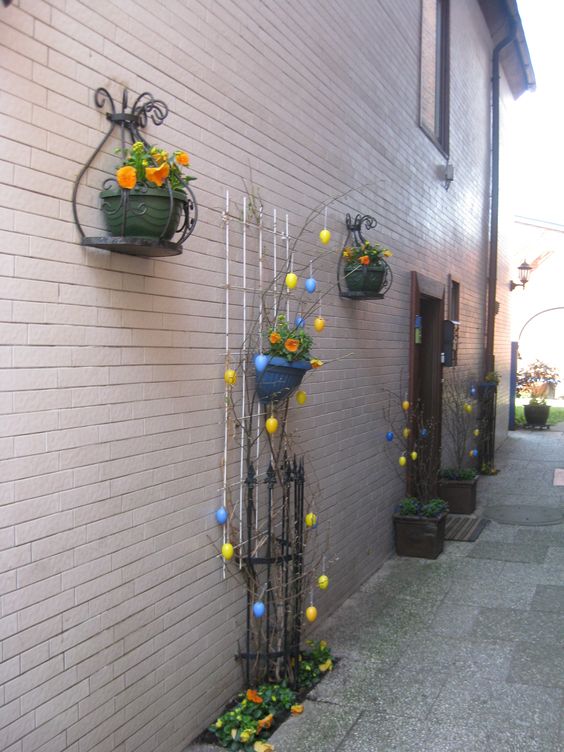 Lovely Easter garden decoration with the flower pot on iron railing and cover some branches, hang yellow and blue Easter eggs on all the branches.